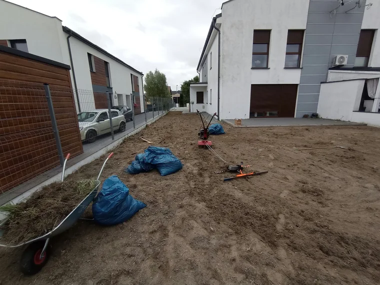 Oczyszczone podłoże przy budynku, taczka, worki z roślinnością i sprzęt ogrodowy